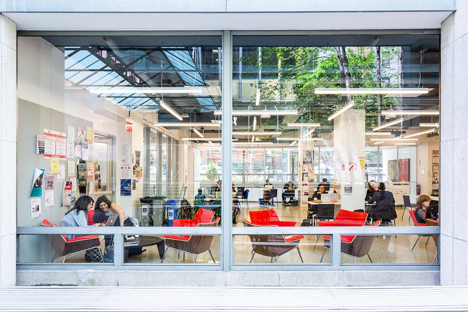 从落地窗可以看到新学校繁忙的朗咖啡厅. 几个学生坐在红椅子上，分组或单独学习.