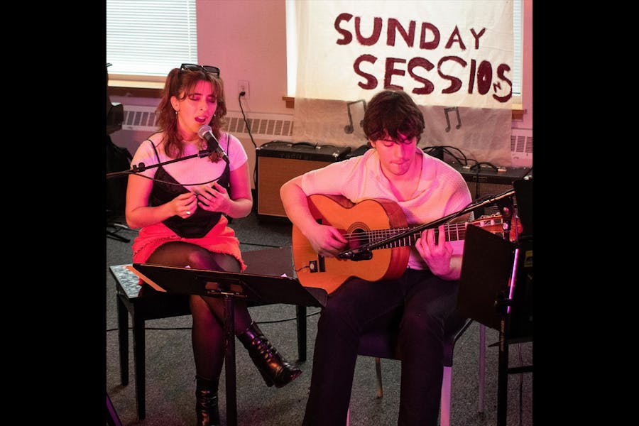 Two students perform, one singing and one accompanying on guitar