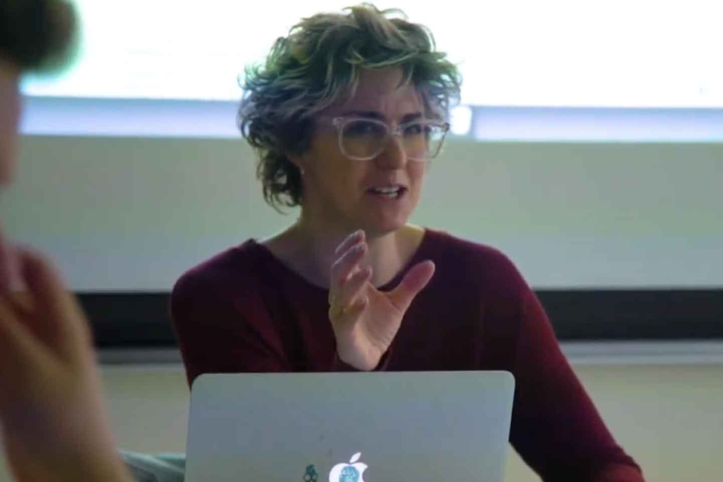 Medium shot of instructor gesturing as she teaches a class.