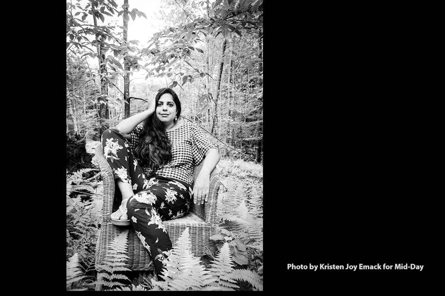 Anjali Khosla sits in a wicker arm chair in a wood of ferns and trees.
