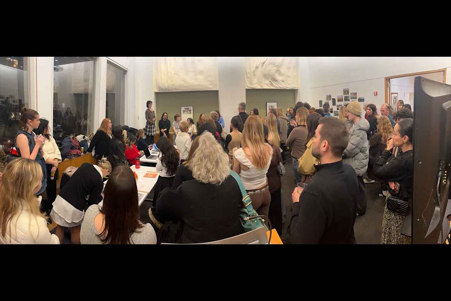 People gathered in a room, watching and listening to students making presentations