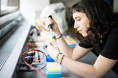 A student uses a pipette to add liquid to a small tube in a laboratory.