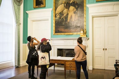 People in a museum photograph a painting on a green wall.
