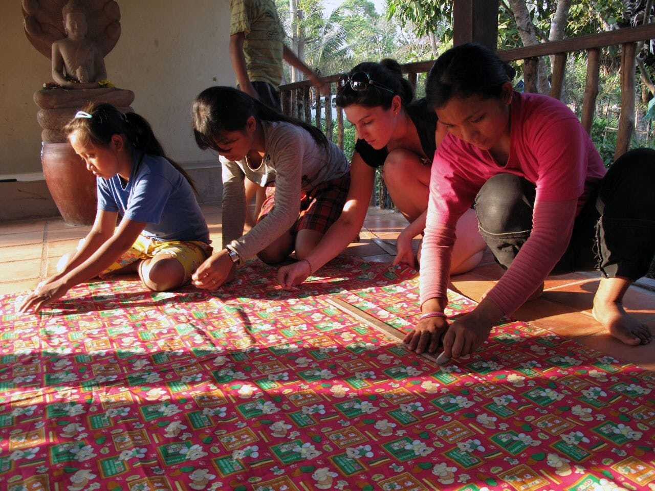 Young people in Cambodia kneel on a cloth with rulers, taking measurements.