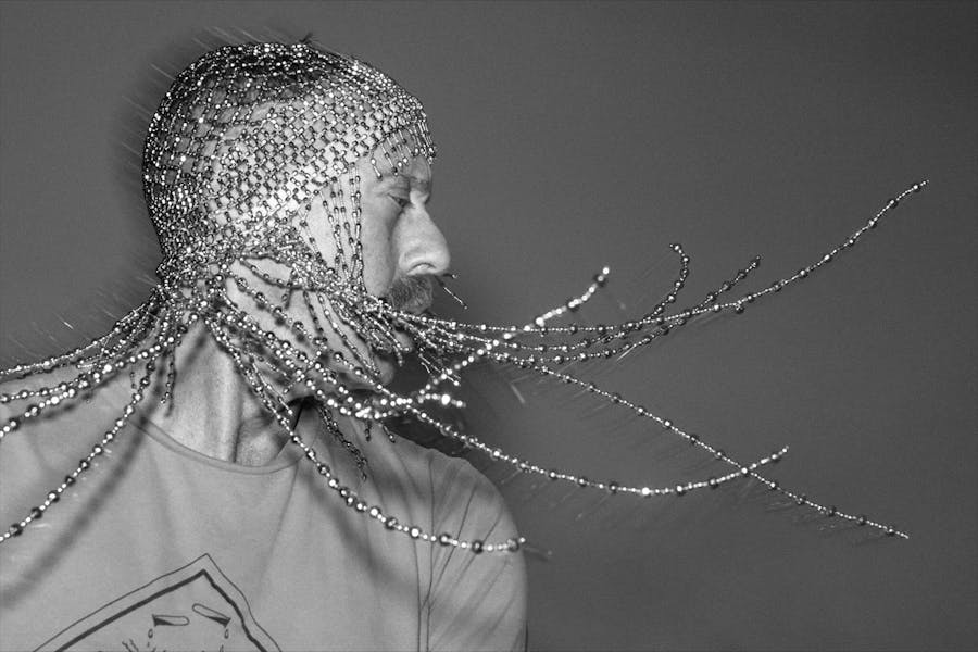 Black and white photo of someone with a beaded headdress swinging lengths of beads.