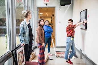 Three students observe a fourth installing artwork in the Lang School Skybridge