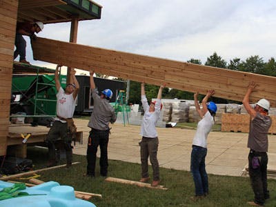 A team of people with hardhats lift a beam together to construct Empower a House.