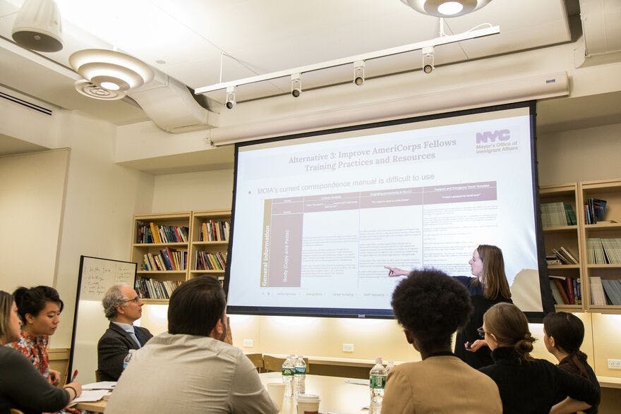 People in a conference room look at a presentation on a large screen.