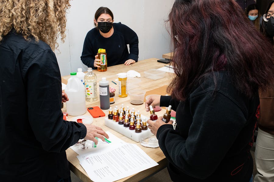 A female faculty member and students around a worktable review notes and work with bottles of natural pigments 