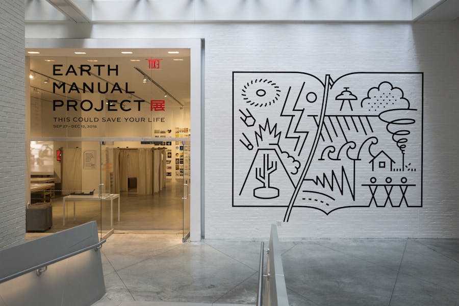 A view of the SJDC gallery with the title Earth Manual Project This Could Save Your Life printed on the glass entrance and a black abstract line drawing mural of environmental elements to the right.