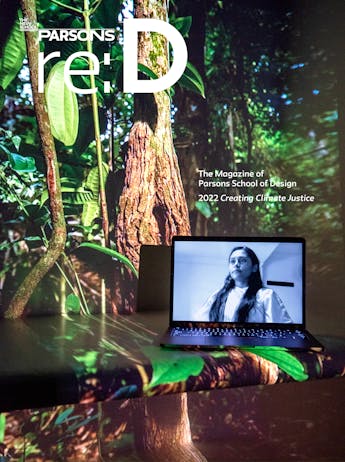 Depicting an art installation, a laptop displays a portrait of a young Latinx woman in black and white, surrounded by lush green jungle foliage; over it appears the words “The Magazine of Parsons School of Design, 2022, Creating Climate Justice”