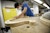A masked student works on a curved wooden piece on a table