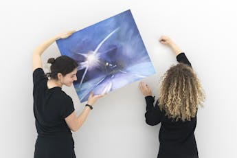 Student and professor install a painting in preparation for an exhibition.