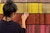 A student with their back to the camera passes a hand over a red and yellow tapestry