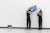 Student and professor with their backs toward the camera mount a painting on a blank white wall.