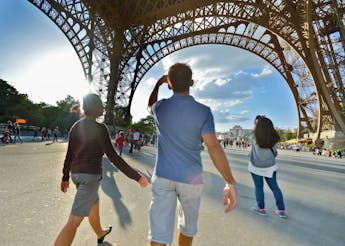 A group of students gather at a sunny hardscape plaza beneath the Eiffel Tower, taking pictures and sightseeing.  