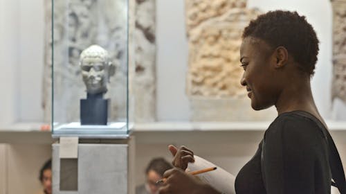 A student admires a sculpture while holding a pencil and paper.