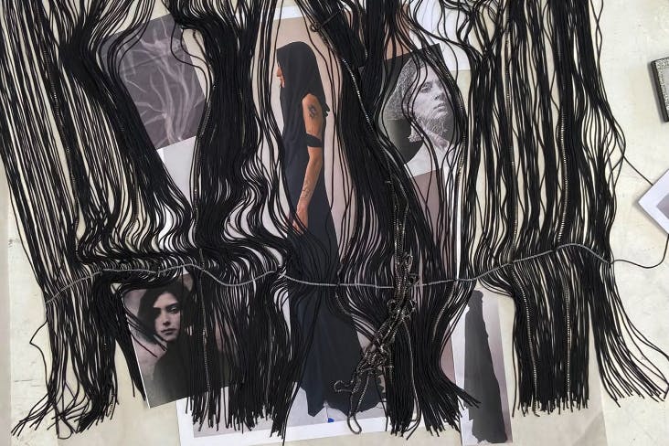Photos hung on a white wall are partially covered by a swath of black fringe.