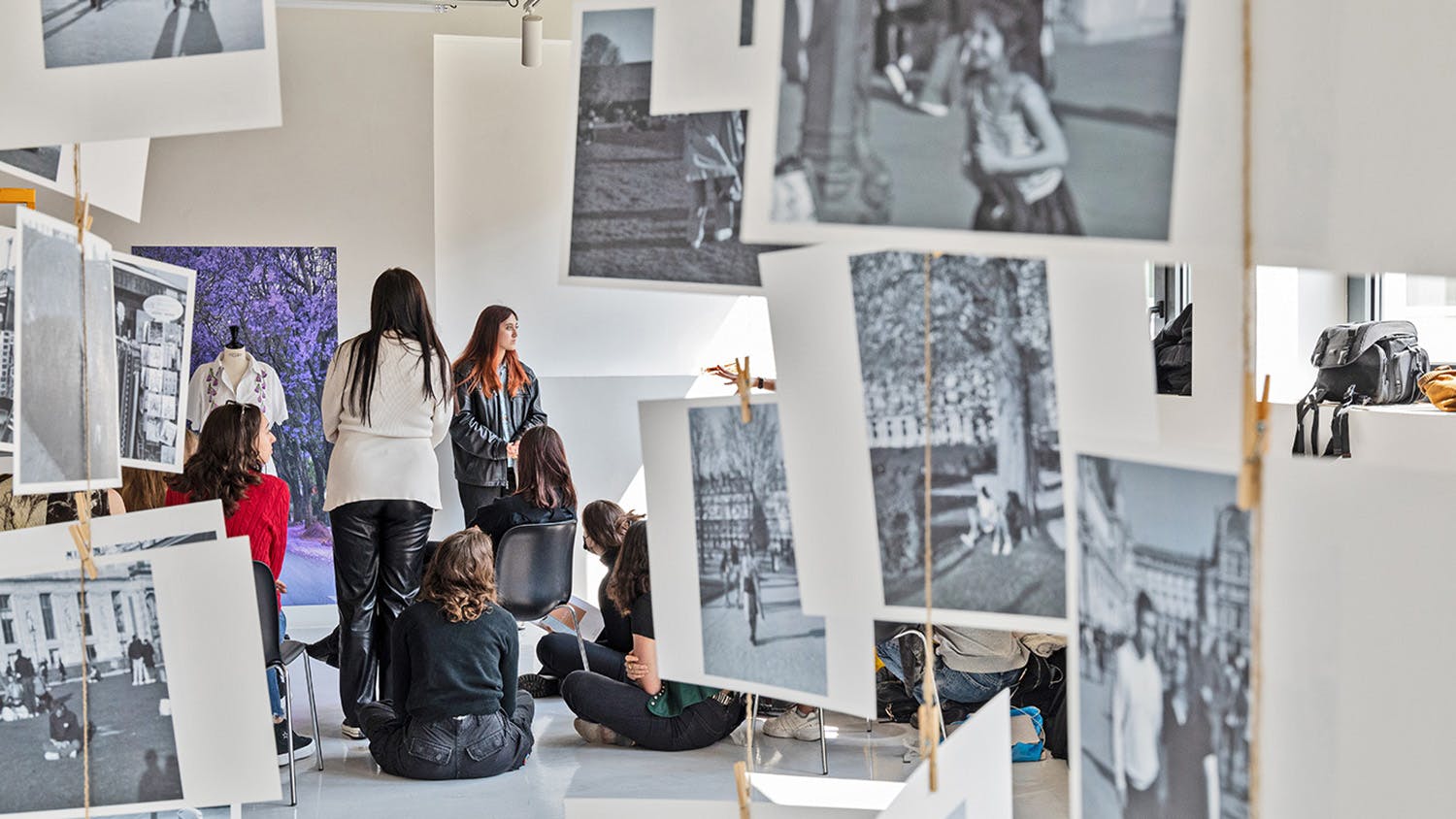 Students sitting and standing, surrounded by work hanging in the room, during a critique.