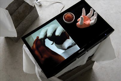Making Skills Hub—a black surface sits on a block, on half of which appears to be a human hand with fingers covered and held in a claw pose near a bowl of caviar next to a video screen.