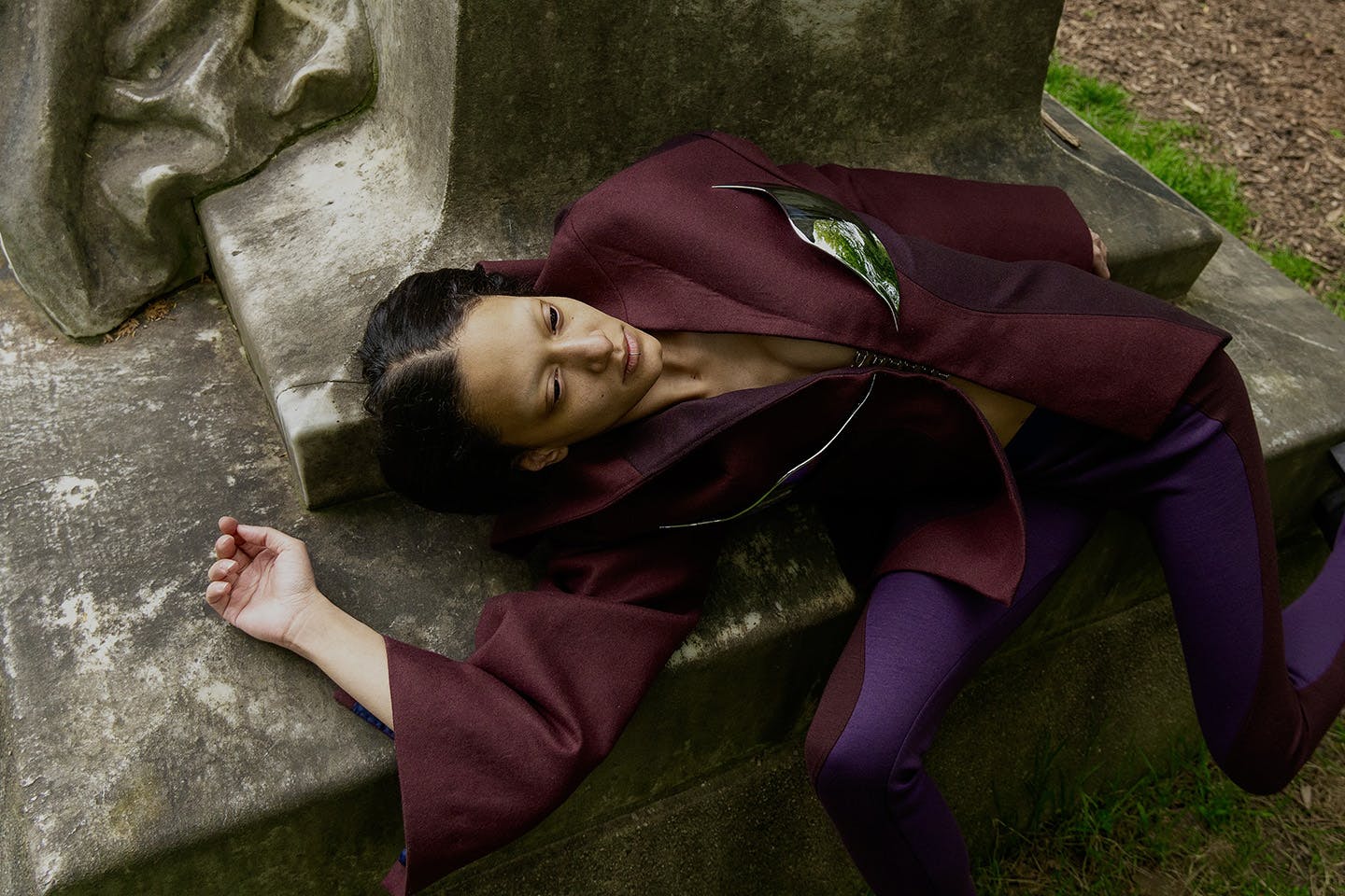 Wendy Kuo Mugler poses lying down at the foot of a statue wearing a purple and burgundy outfit.