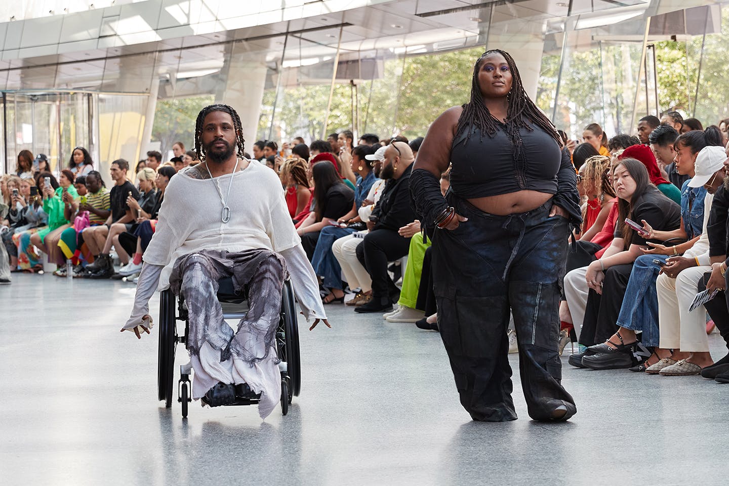 Photo of models, one in a wheelchair, the other on the runway, wearing fashion designs from an alum.
