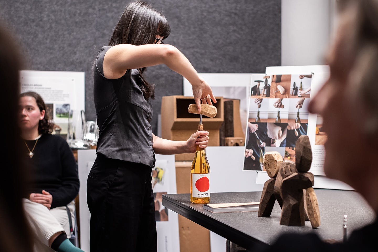 Linnea (Hanna) Wallin demonstrates her wine cork remover crafted from a sturdy, high-density cork material as the crit panelist judges look on.