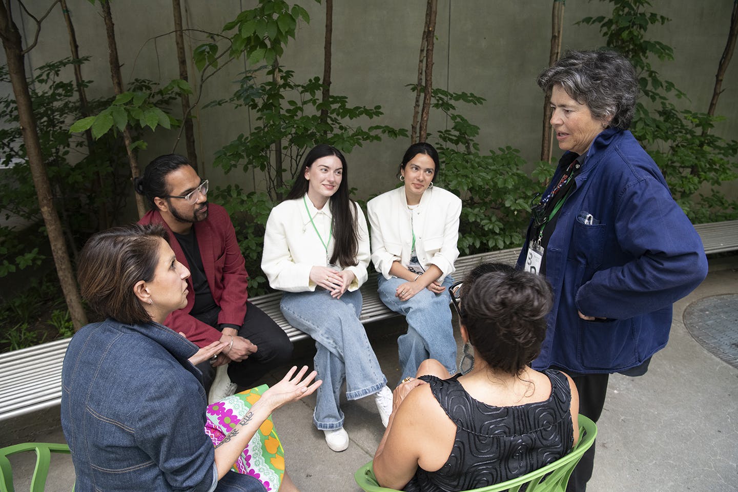 In a courtyard, a woman in a jean jacket and one in a blue jacket converse while students Irmak Senyurt and Lucía Jaramillo and another woman and a male professor listen.