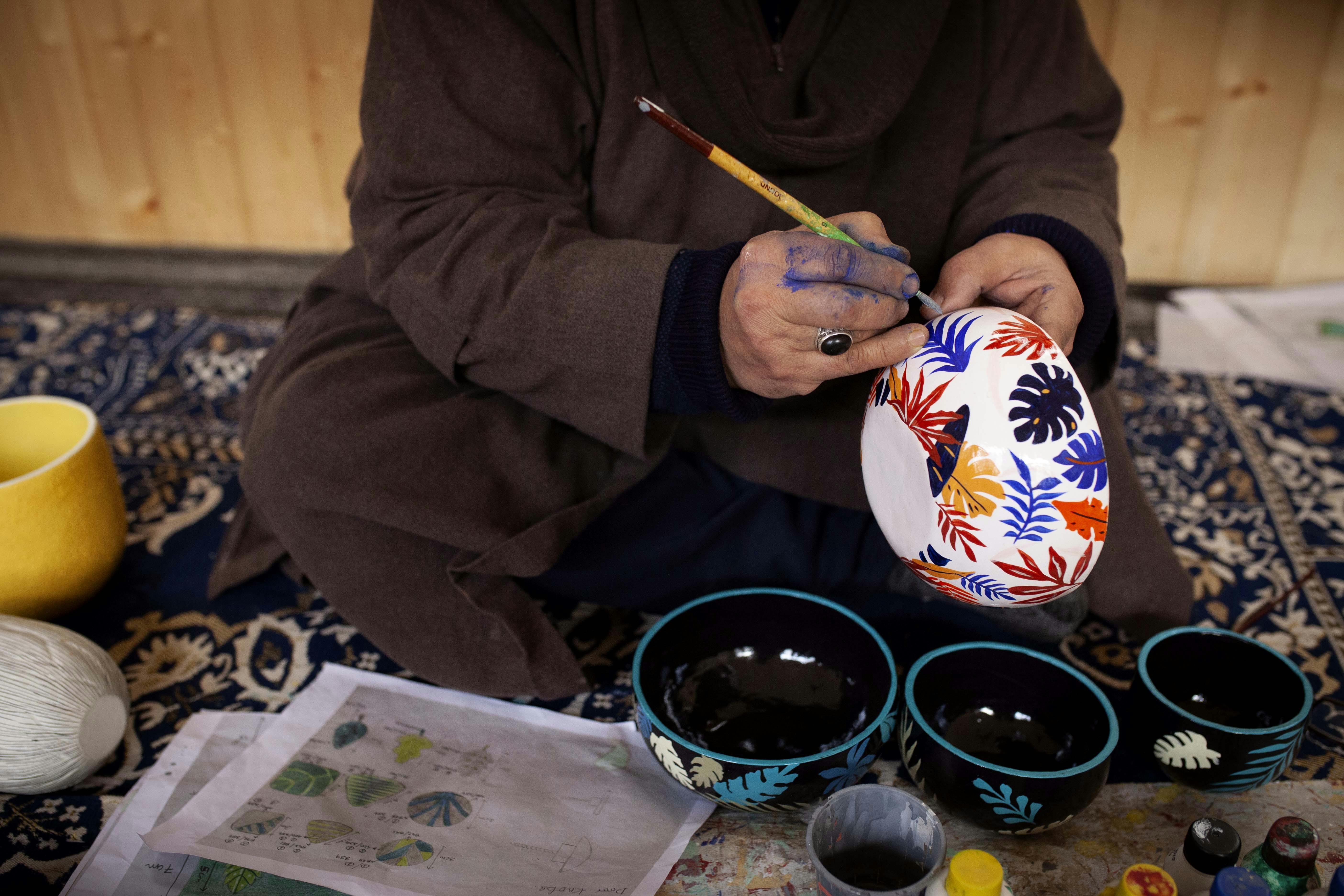 An artisan hand-paints a selection of papier-mâché home decor items.