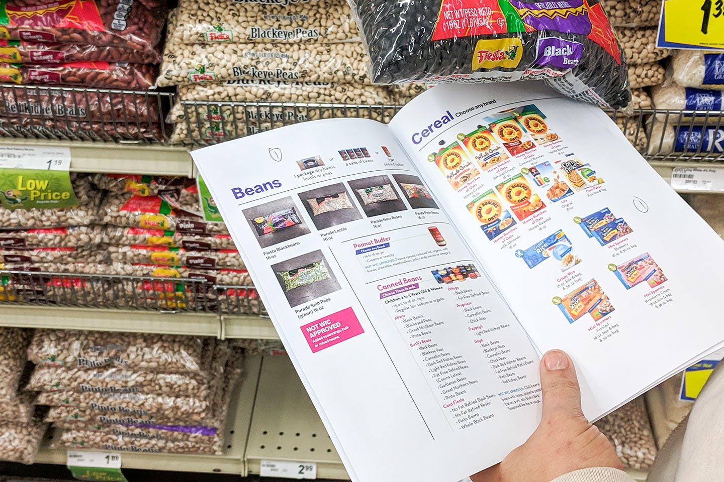 A hand in a grocery store aisle holds an in-store product guide with visuals in front of shelves of beans