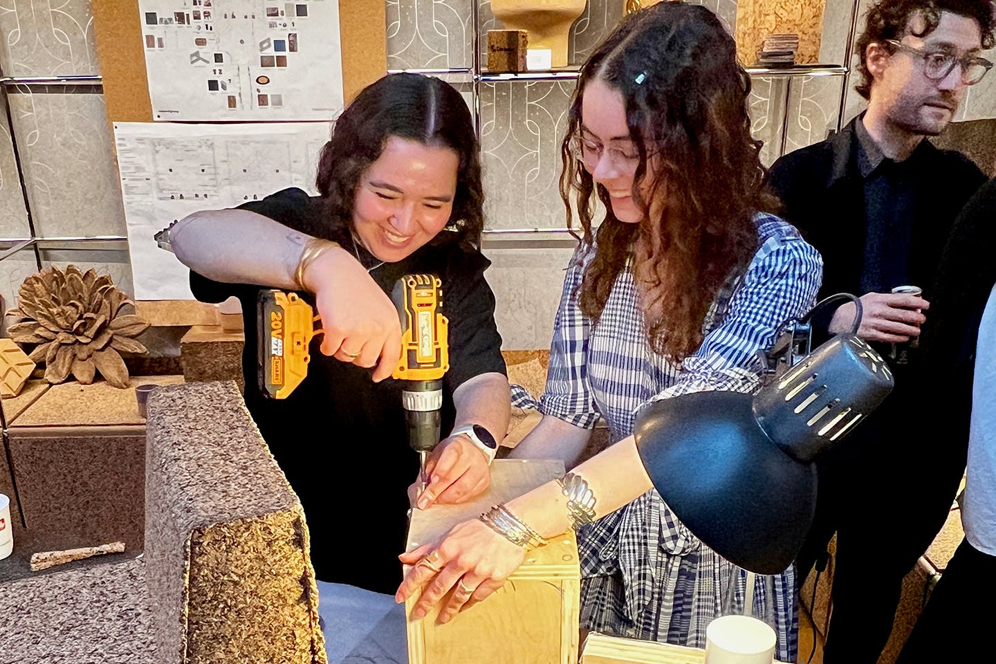 Students Carolina Miñana and Emily Quinn lead a cork-molding workshop at Casa Cork in Milan, demonstrating techniques to a group of participants around a worktable.