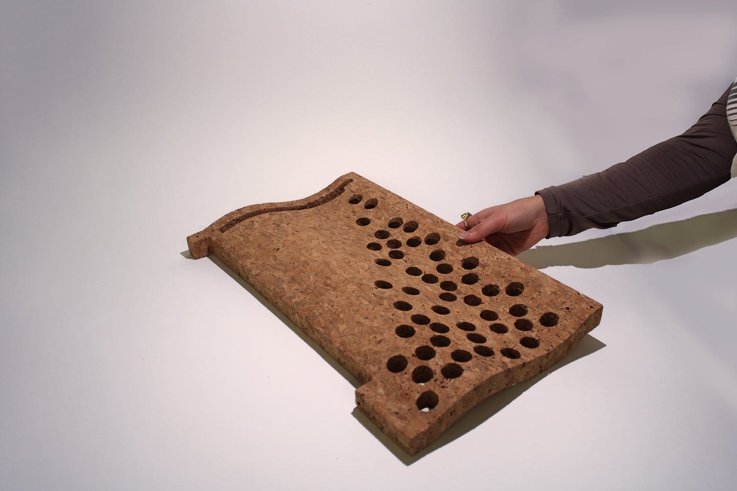 A hand extends to display Rucha Kumthekar’s Tapeçaria—a set of perforated, molded cork tiles inspired by traditional Portuguese ceramics.