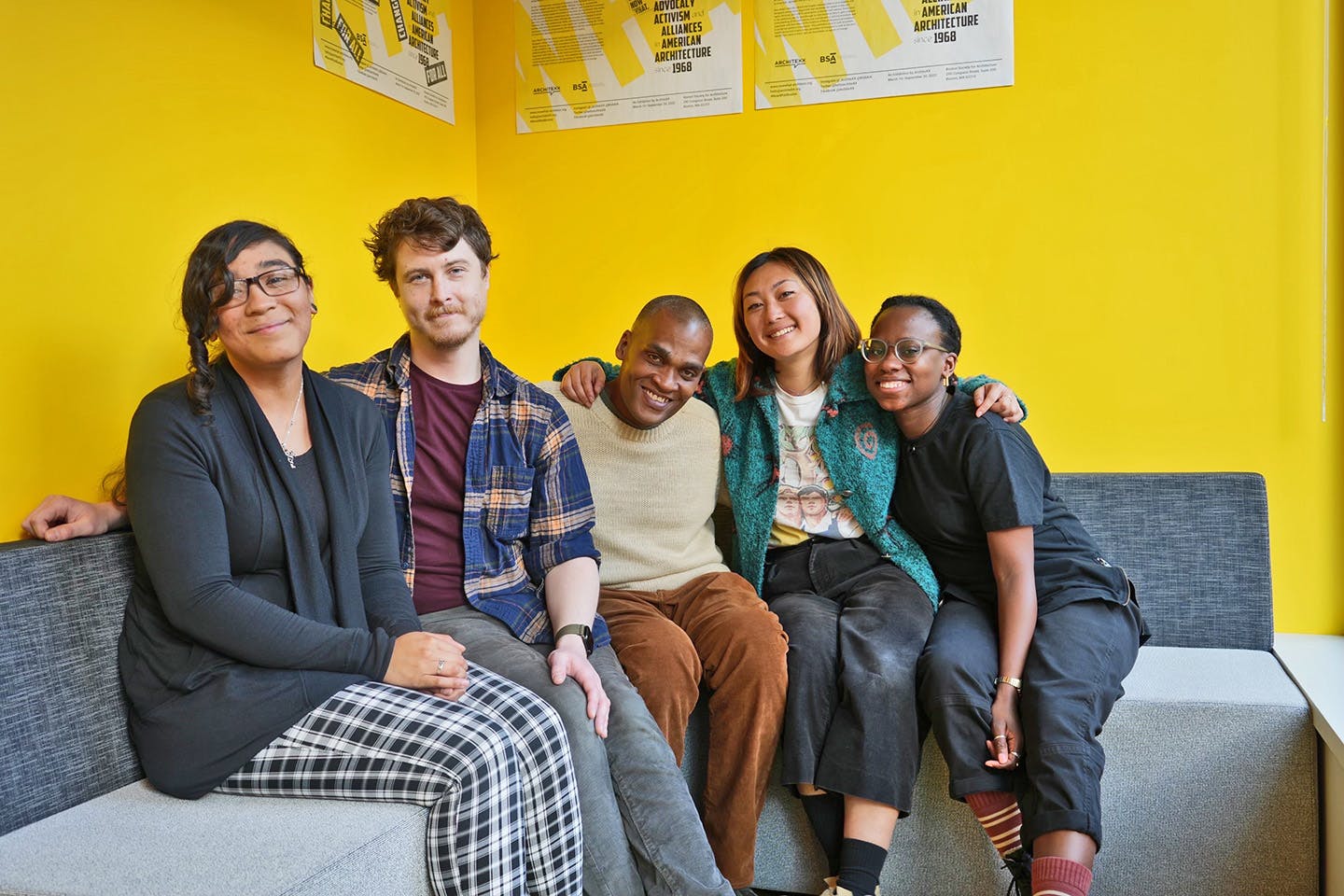 Dorsainvil posing with five members of the SYITF Collective on a couch in front of a yellow wall.