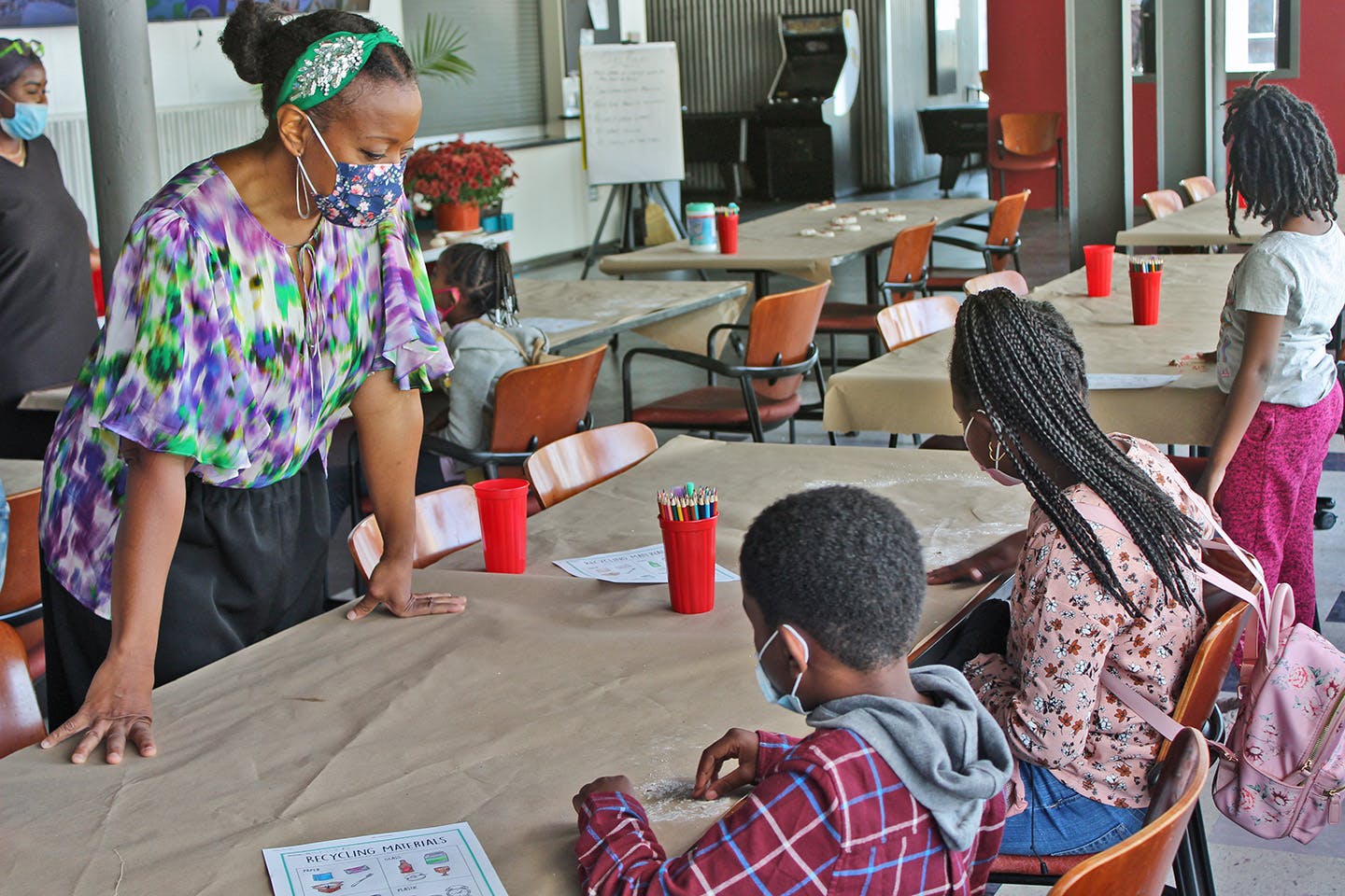 Reese standing over a table teaching three young adults in her free art class, all of them masked.