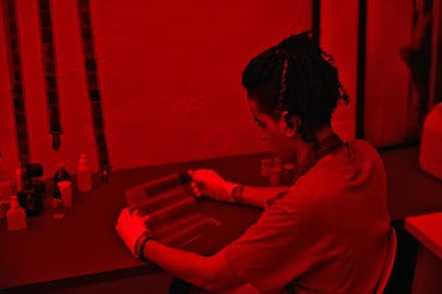 A student developing a photograph in the red light of the dark room.