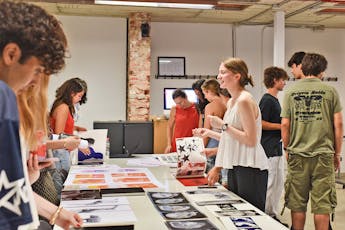 Students surround a gallery table with art and books on it.