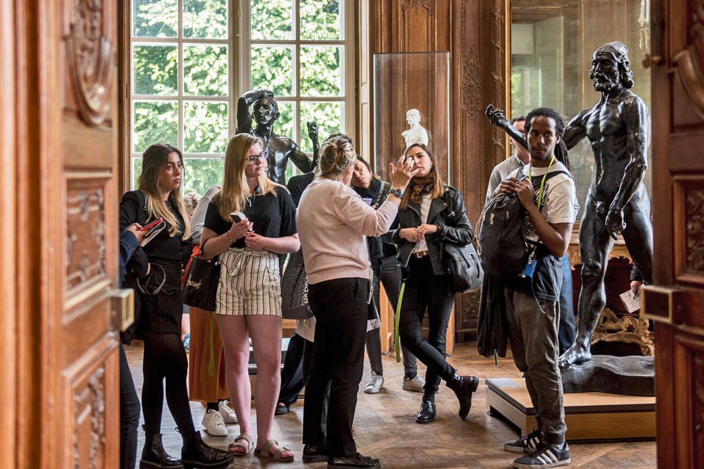 Students stand in a semi-circle, facing a lecturer among sculptures by Auguste Rodin at the Musée Rodin in Paris.