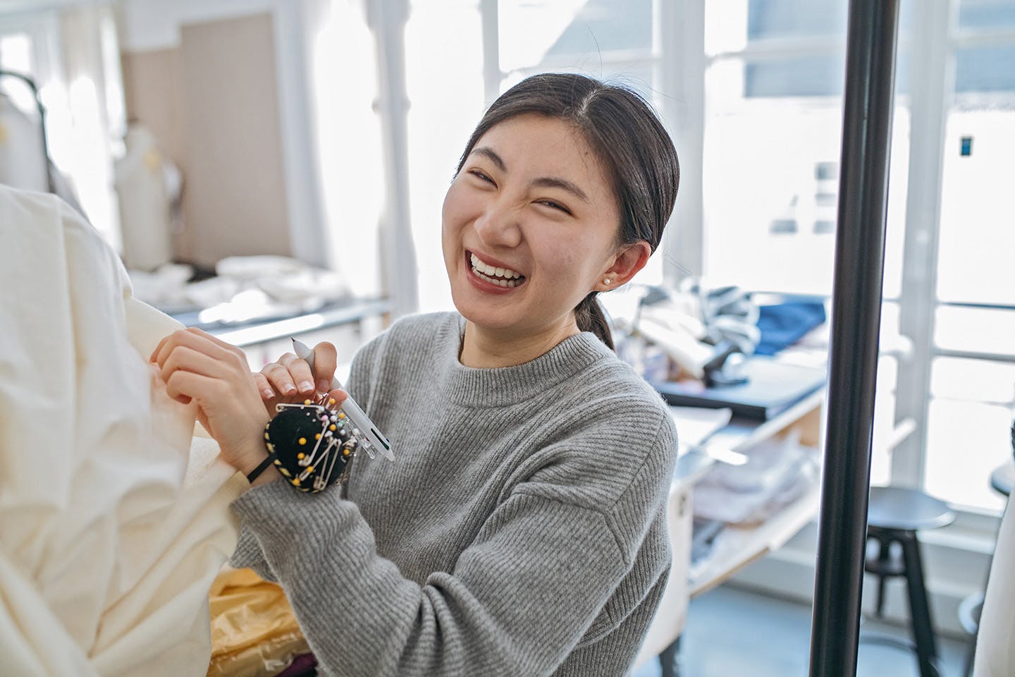 A student laughing while working on a garment with pins and a pen.