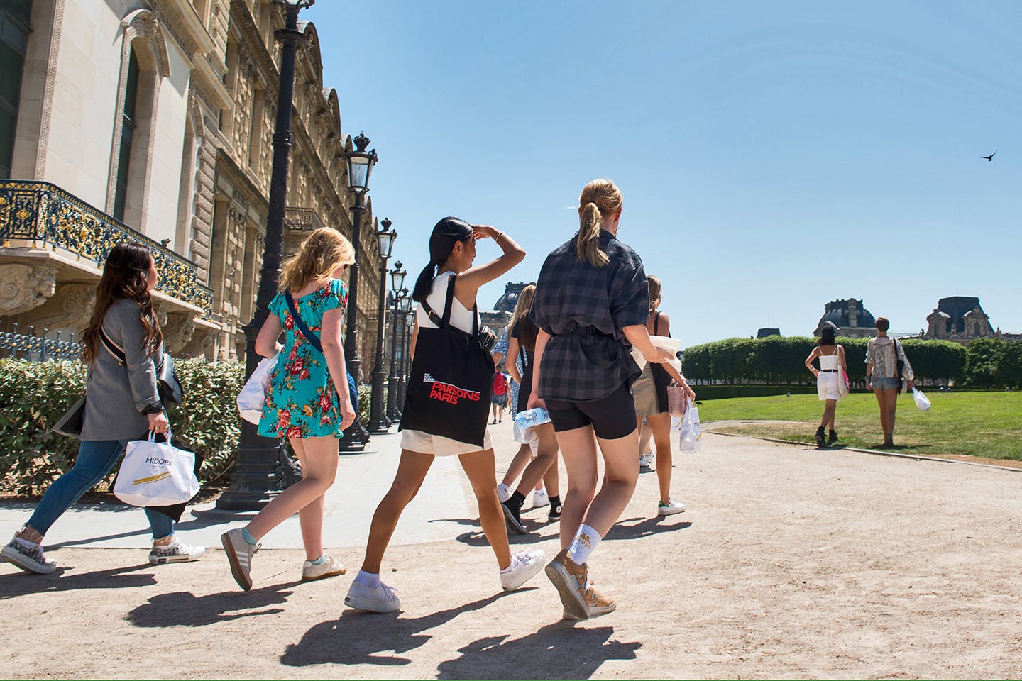 Students walk diagonally across the camera, away from a building and towards a lawn in Paris.