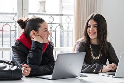 Two students talk in a classroom.