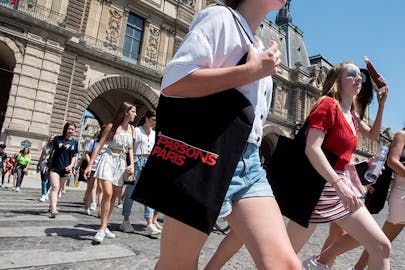 Students walk outside on a sunny day in Paris. A student wears a Parsons Paris tote bag.