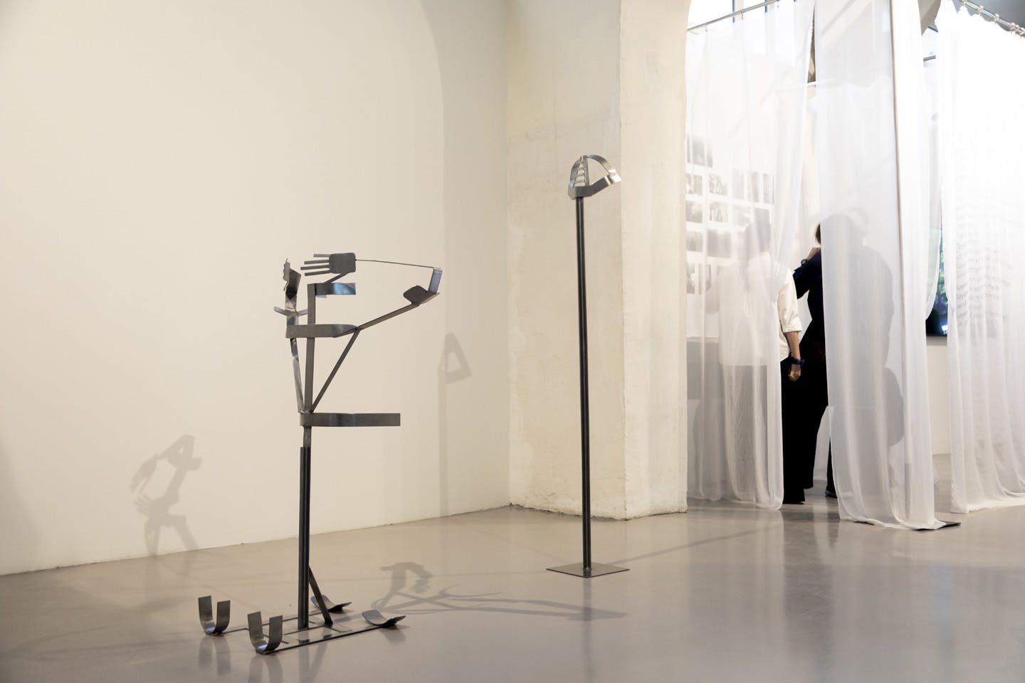 Abstract metal sculpture installation beside sheer white curtains