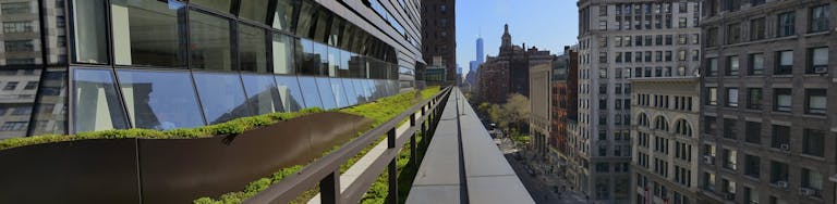 University Center green space, with Center windows on left, and Fifth Avenue on the right. Blue sky reflected in windows.