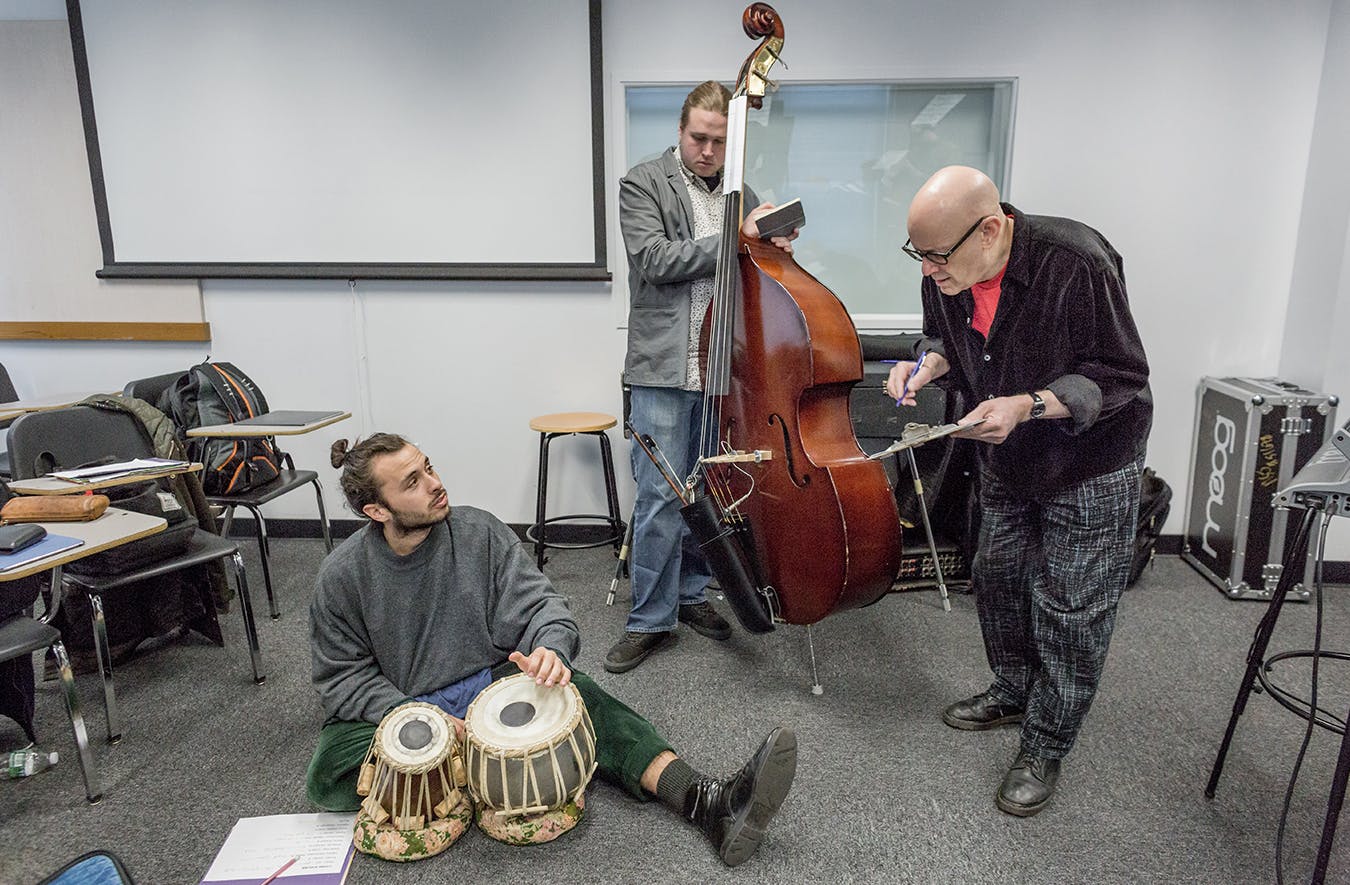A student with hand drums and another with an upright bass listen to their professor give feedback.