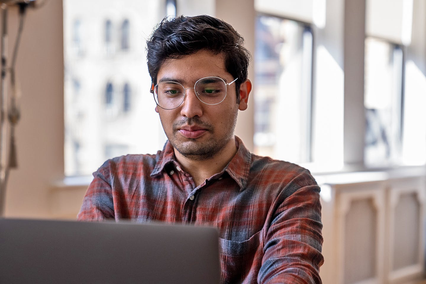 A bespectacled student works at a laptop