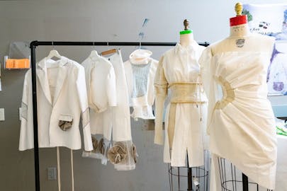 White sustainable garments are hanging on rack and wire mannequins. 