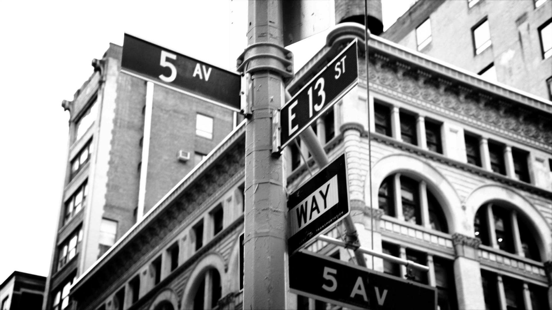 A black and white photo of the street signs at the intersection of Fifth Avenue and 13th Street.