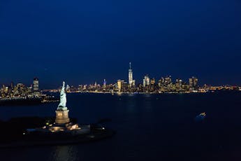 A view of the Statue of Liberty and the New York City skyline at night.