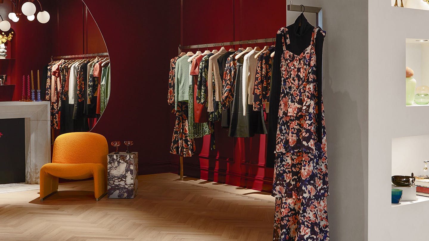 The interior of Tanya Taylor's Madison Avenue store, showing clothing hanging in front of burgundy walls, a large circular mirror, and a yellow chair next to a small marble table.