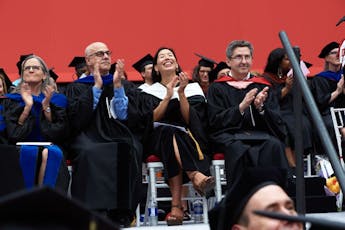 Seated University faculty and administrators applaud during commencement ceremony
